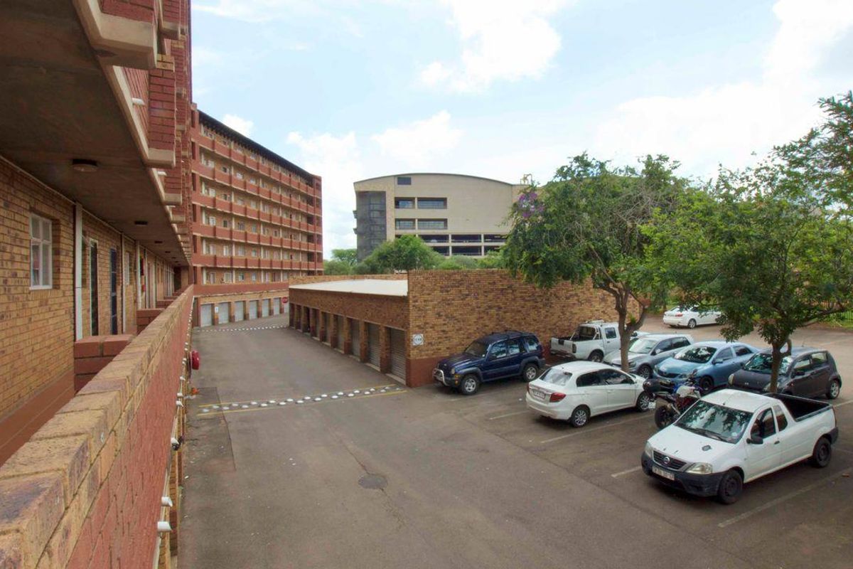 Exterior view of the apartment complex showing the brick facade, covered parking bays, and open parking area.