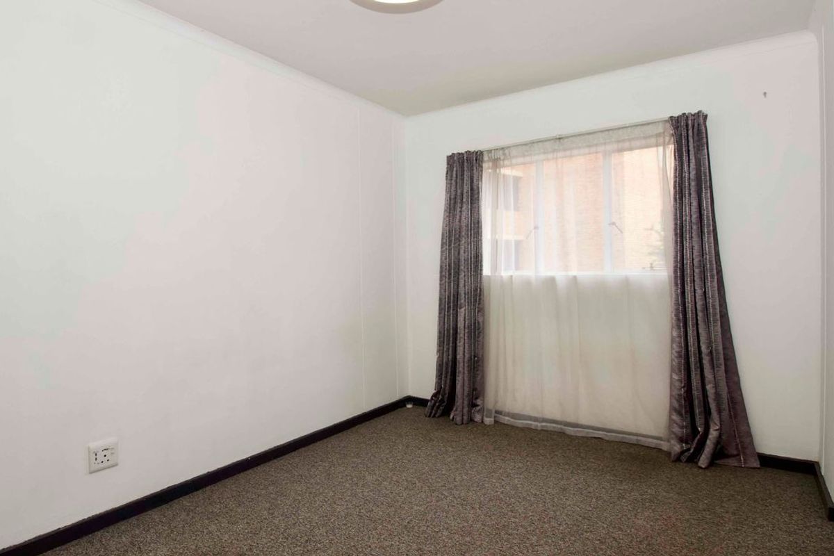 A clean, empty bedroom featuring neutral walls, dark carpeting, and a window with installed curtain tracks.