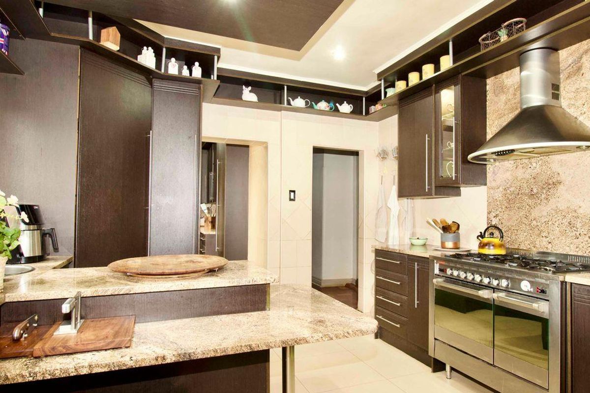 A well-appointed kitchen featuring dark wood cabinetry, granite countertops, a built-in gas stove with extractor fan, and tiled flooring.