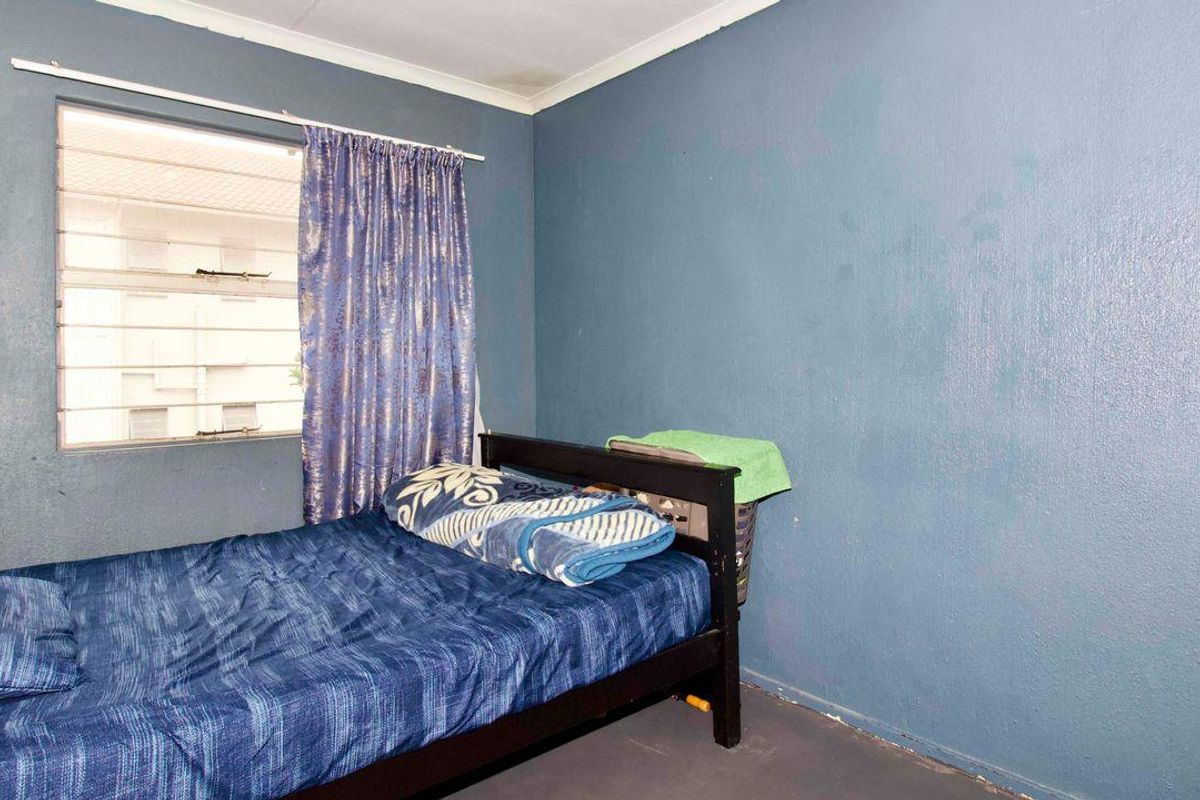 A bedroom featuring blue painted walls, a louvered window, and basic flooring, offering a functional space ready for cosmetic updates.