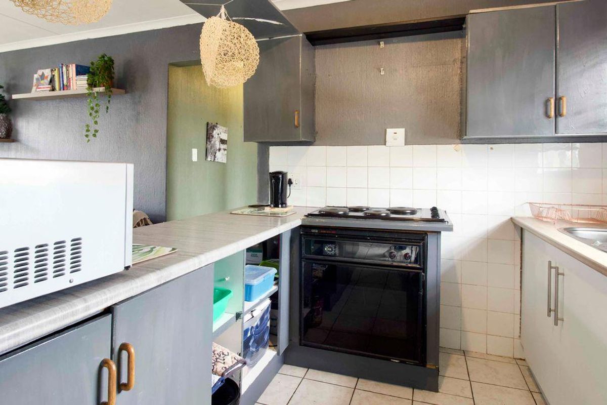A compact kitchen featuring built-in cabinetry, a freestanding oven with hob, tiled backsplash, and a stainless steel sink.