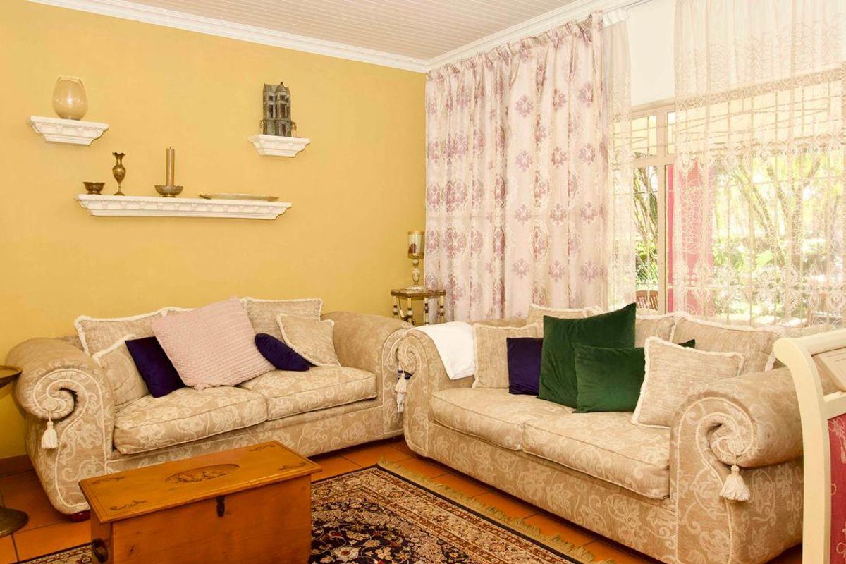 A comfortable living room featuring tiled flooring, large windows with natural light, and classic wall-mounted shelving.