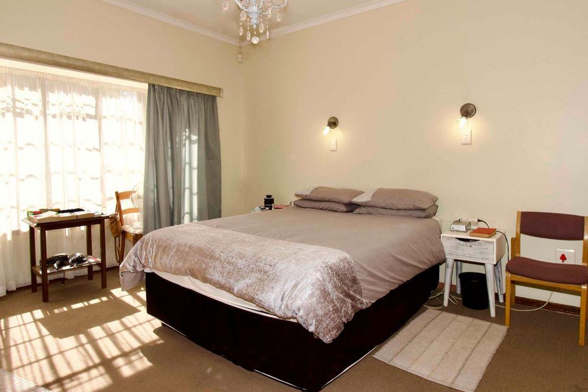 A bedroom featuring carpeted flooring, wall-mounted lighting fixtures, and a large window with curtains allowing natural light.