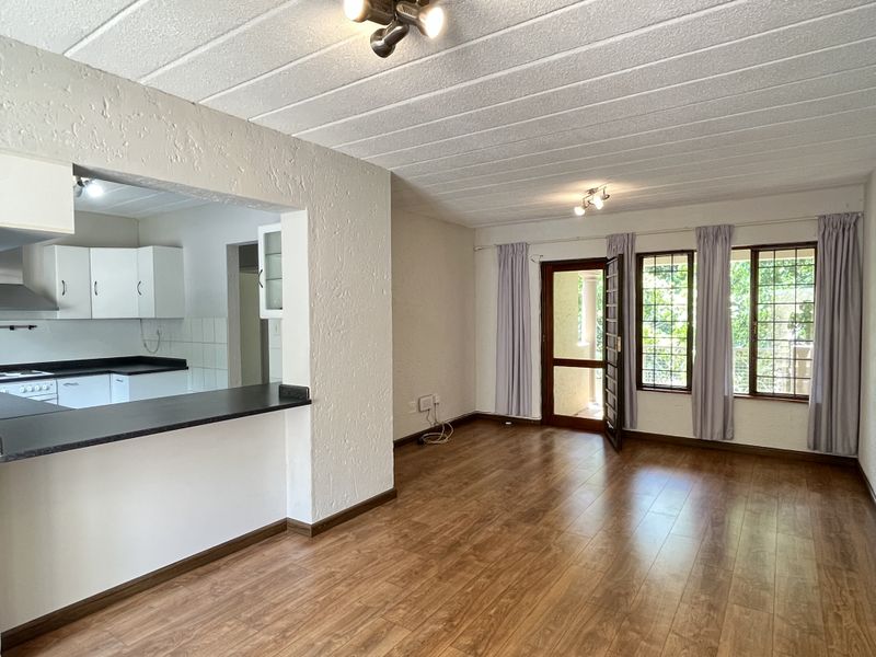 Open-plan living area featuring laminate flooring, a breakfast bar, and a functional kitchen with built-in cabinetry and appliances, leading to an outdoor balcony.