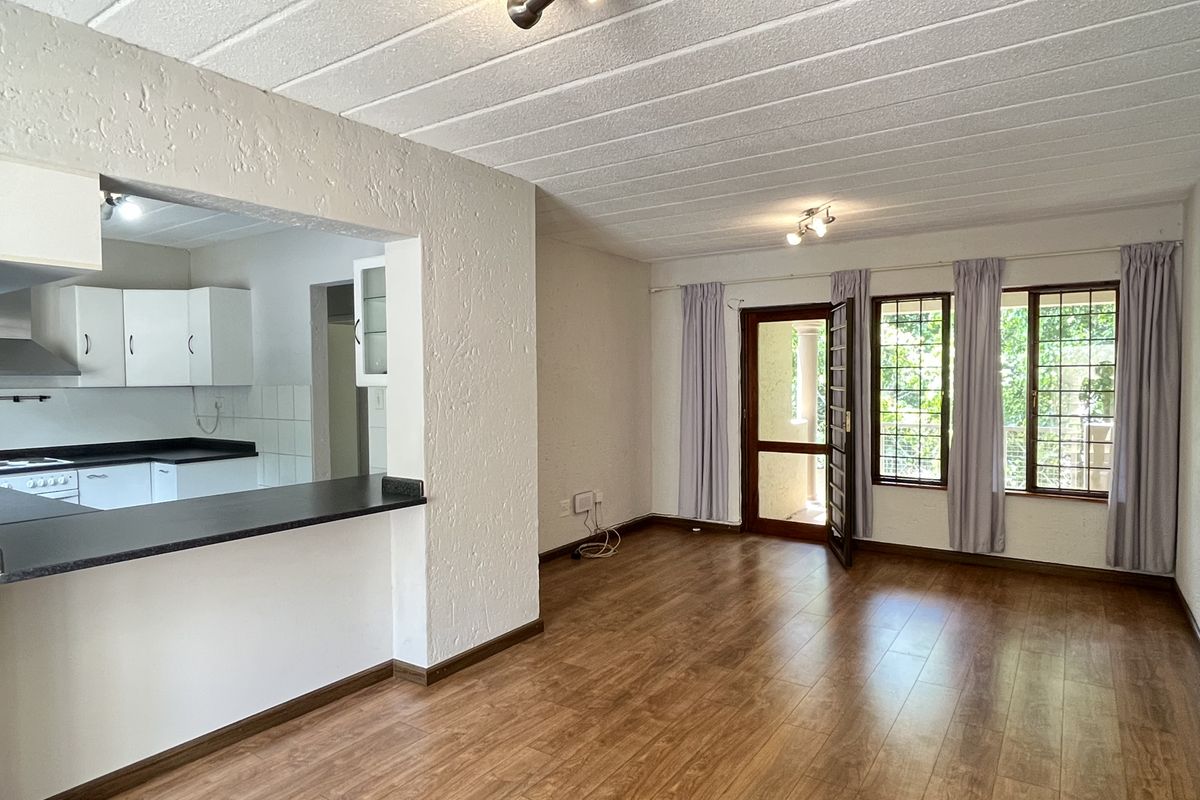 Open-plan living area featuring laminate flooring, a breakfast bar, and a functional kitchen with built-in cabinetry and appliances, leading to an outdoor balcony.
