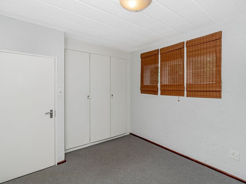 A clean, empty bedroom featuring neutral textured walls, grey carpeting, and ample built-in cupboard storage space.
