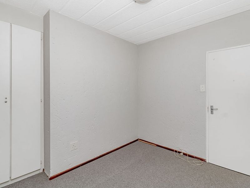 An empty bedroom featuring built-in cupboards, textured walls, and carpeted flooring, offering a blank canvas for personalization.
