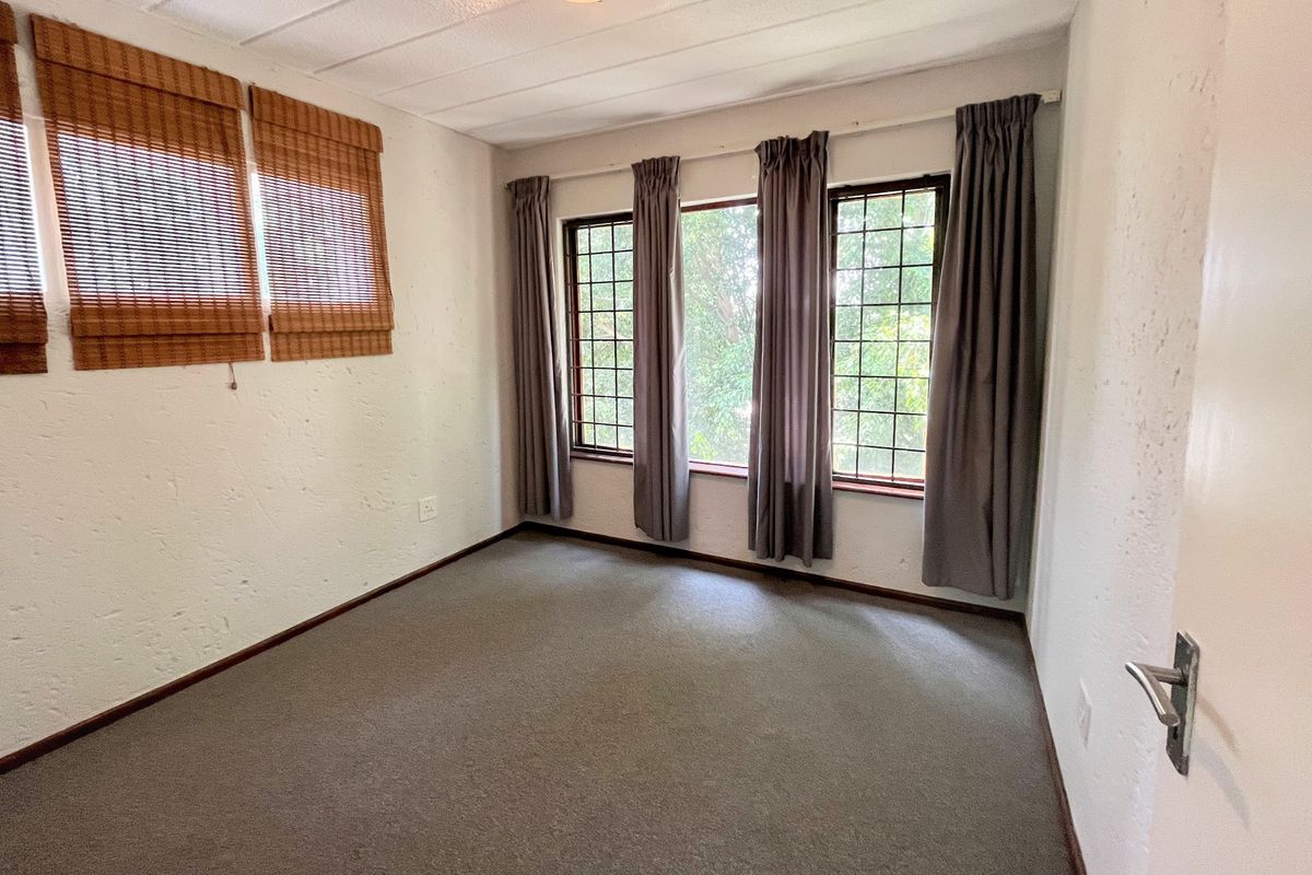 A bright, empty bedroom featuring carpeted flooring, textured walls, and large grid-pattern windows that provide natural light.