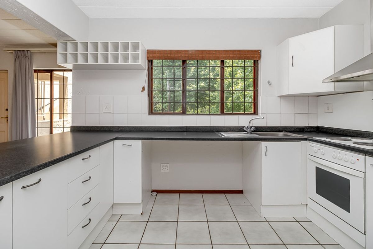 A functional kitchen featuring white cabinetry, dark laminate countertops, a built-in oven with hob, and tiled flooring, offering a clean and practical workspace.