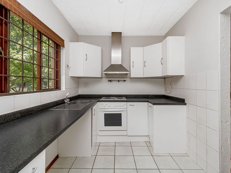 A functional kitchen featuring white cabinetry, dark laminate countertops, a built-in oven with extractor fan, and tiled flooring with a large window.