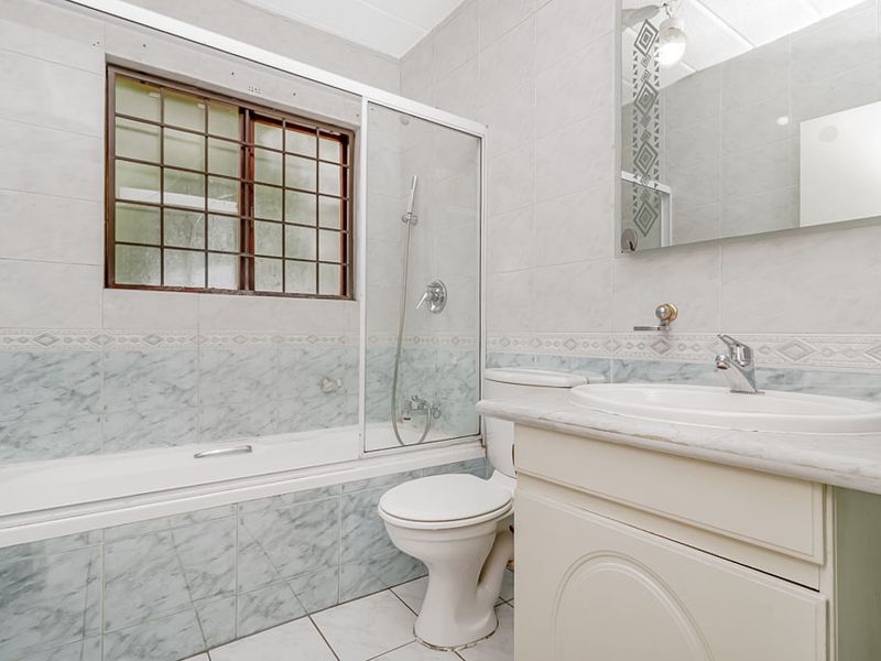 A functional bathroom featuring a built-in vanity, ceramic basin, toilet, and a combined bathtub and shower unit with tiled finishes.