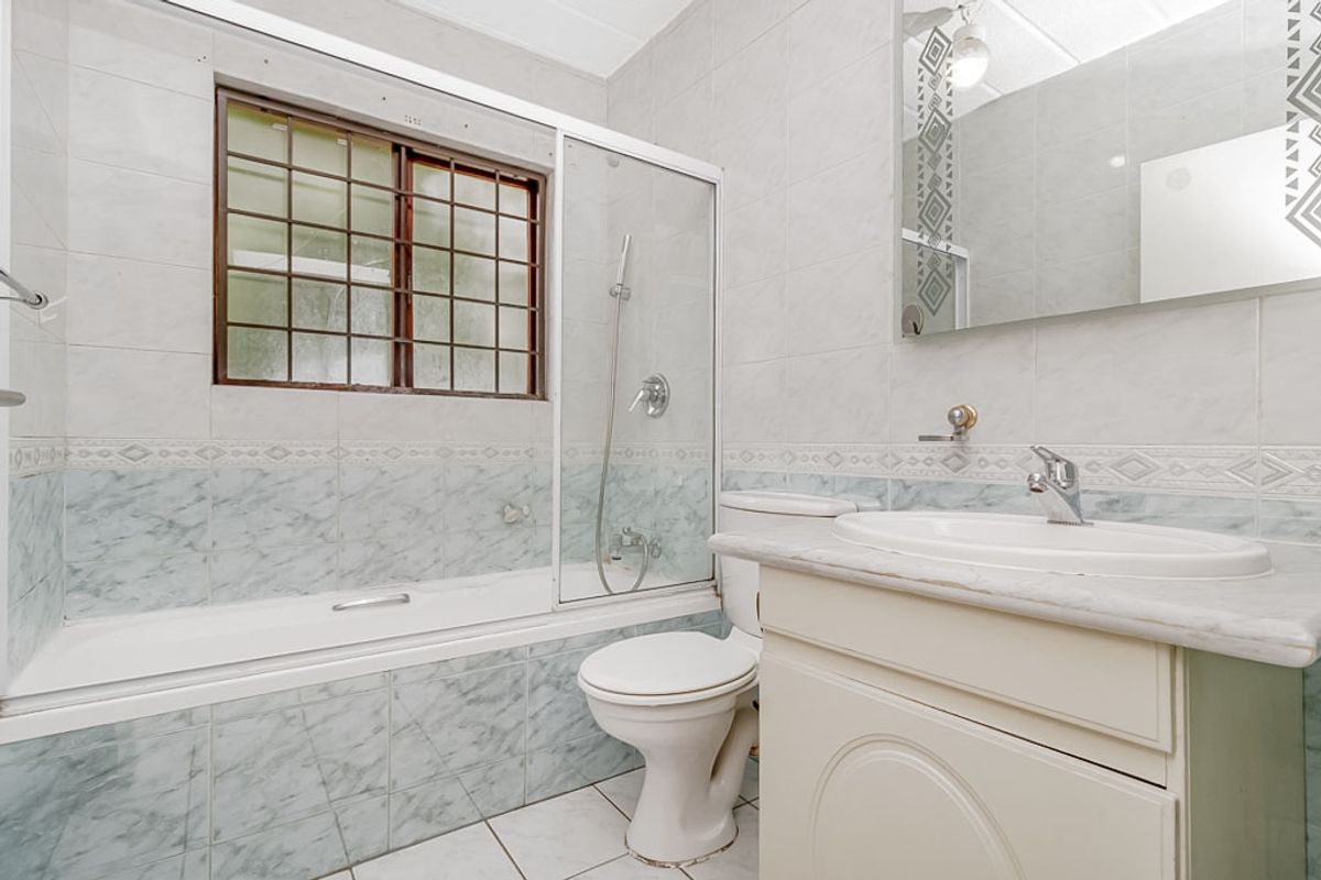A functional bathroom featuring a built-in vanity, ceramic basin, toilet, and a combined bathtub and shower unit with tiled finishes.