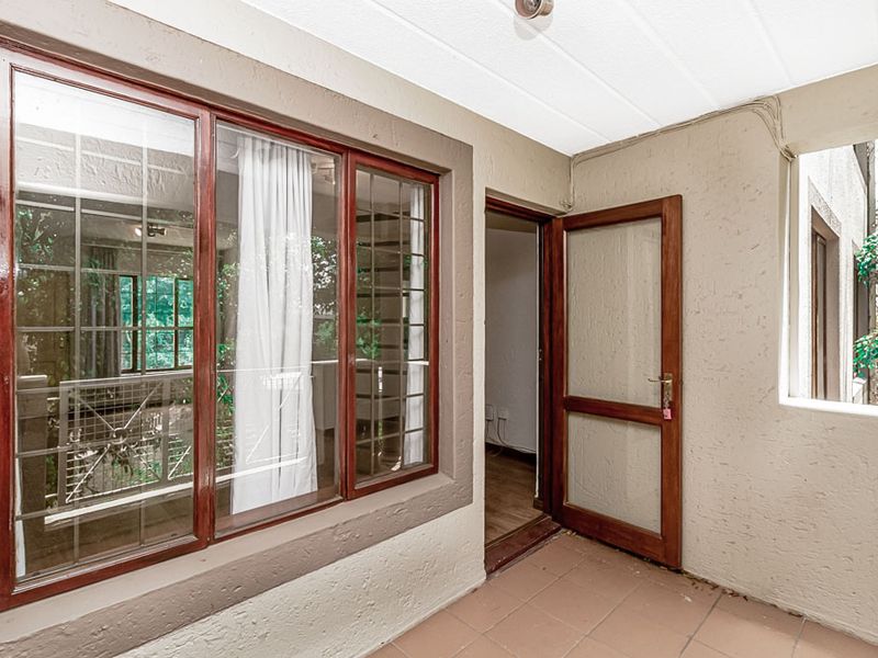 A covered balcony area featuring tiled flooring, timber-framed windows, and a matching timber door, providing a functional outdoor transition space.