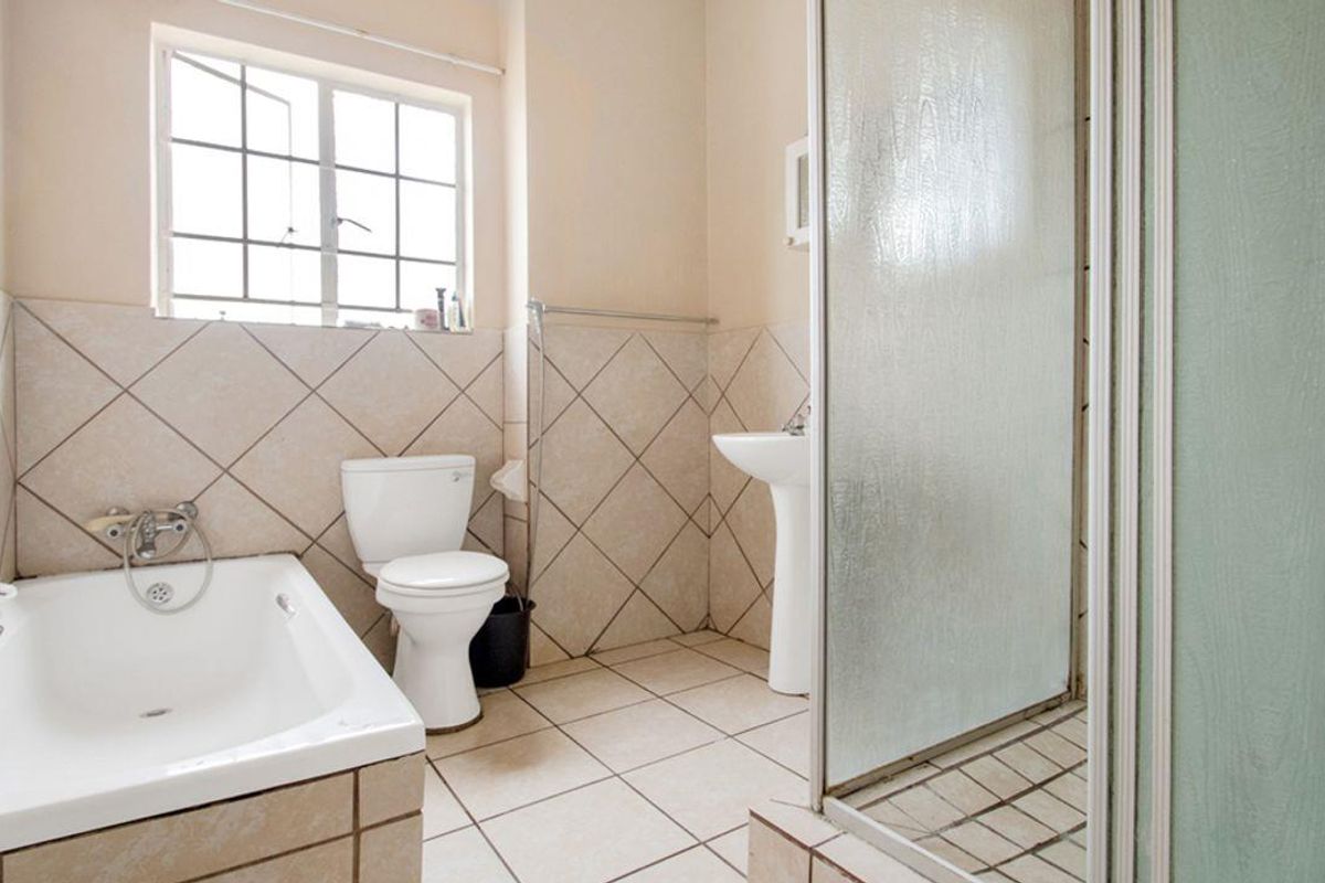A functional bathroom featuring a bathtub, separate shower enclosure, pedestal basin, and toilet with neutral wall and floor tiling.