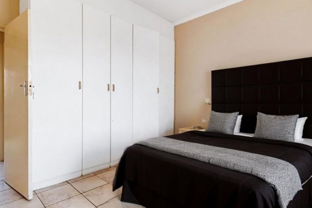 A bedroom featuring built-in cupboards and tiled flooring, with an adjacent view into a bathroom area.