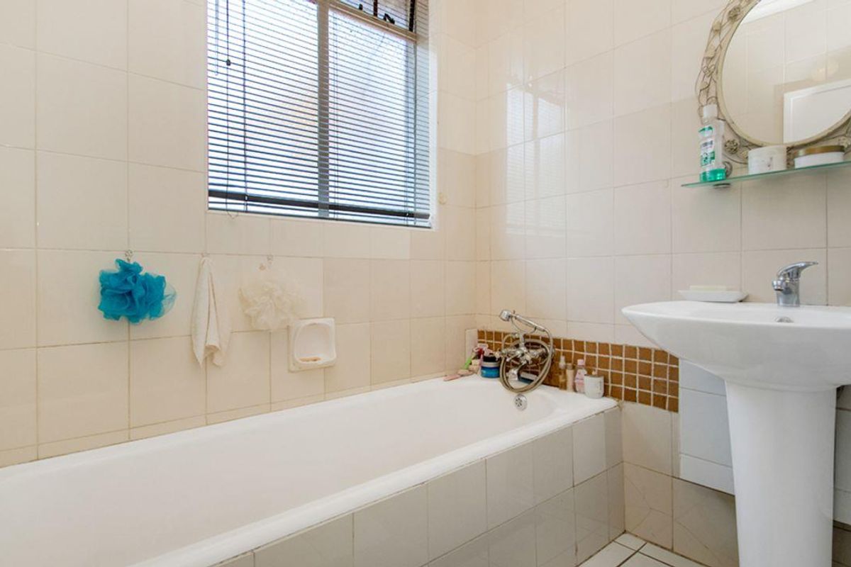 A functional bathroom featuring a white bathtub, pedestal sink, and tiled walls with a window providing natural light.