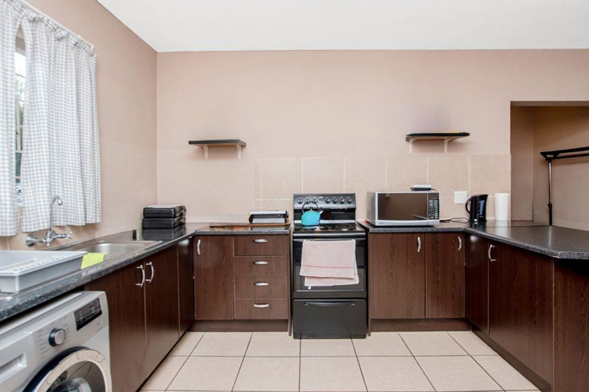 Functional kitchen featuring dark wood-look cabinetry, laminate countertops, tiled splashback, and integrated space for a washing machine.