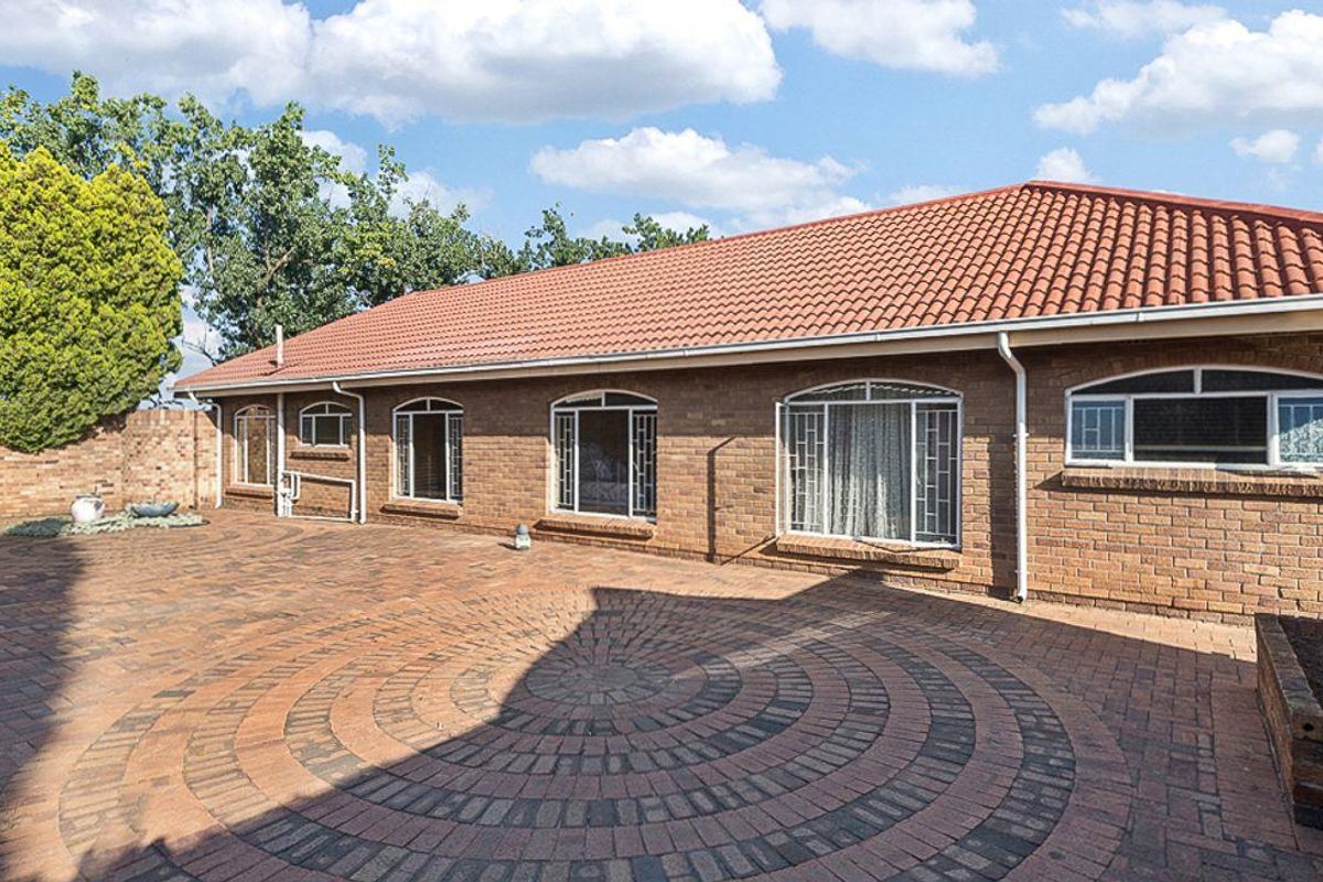 A rear exterior view of a brick house featuring a paved courtyard area with a circular pattern and arched window detailing.