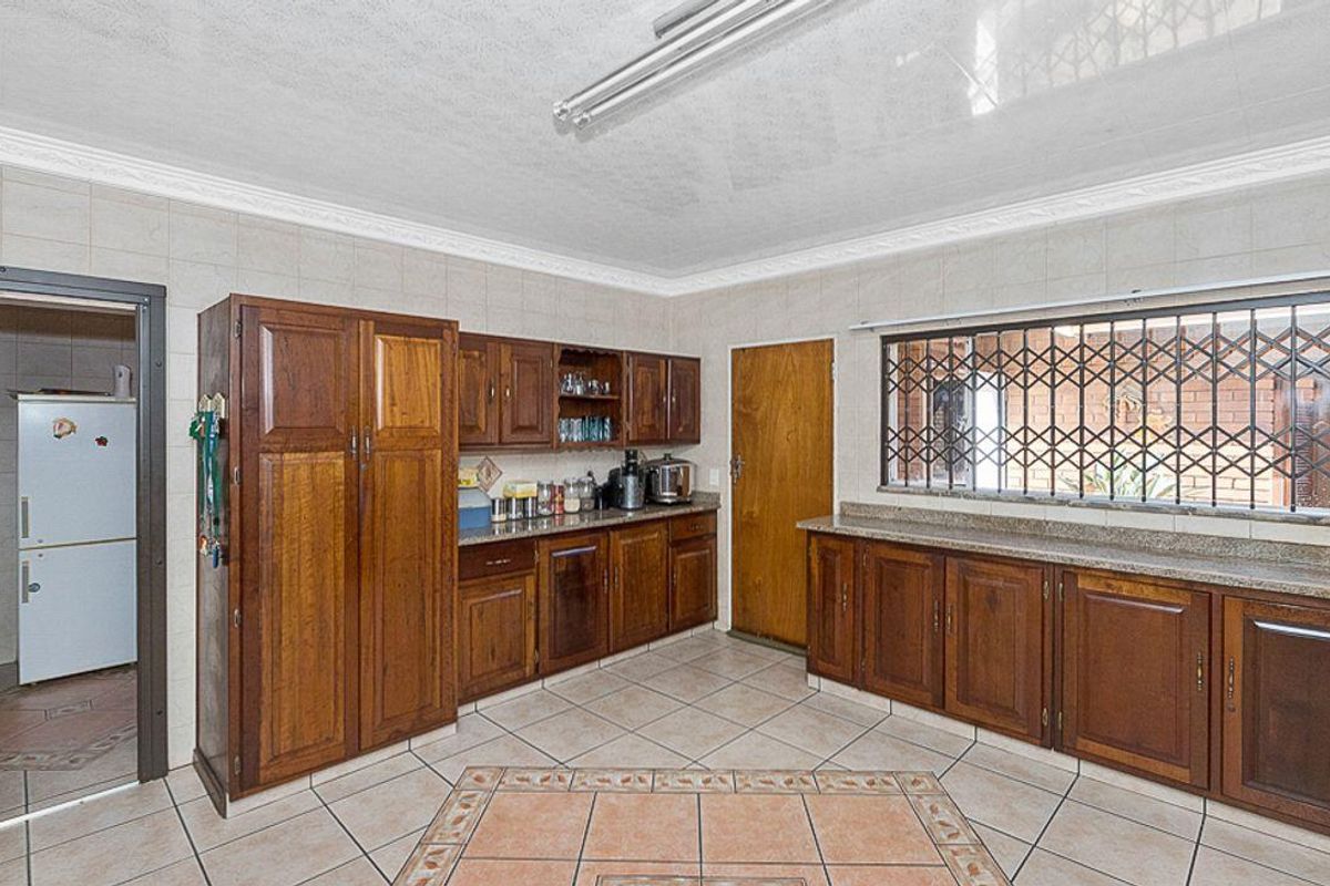 A functional kitchen featuring traditional wooden cabinetry, granite countertops, tiled flooring, and a security gate on the window.