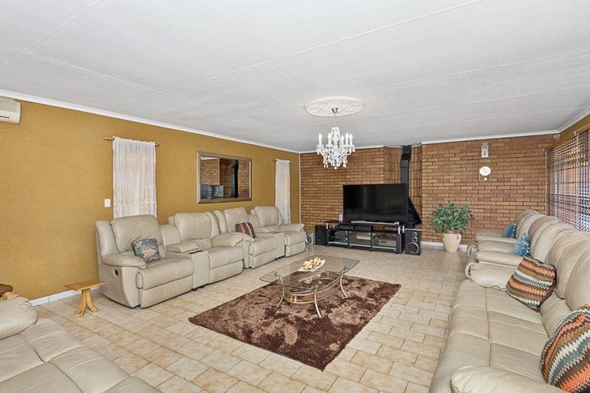 Spacious living room featuring a prominent brick feature wall, a built-in fireplace, tiled flooring, and a ceiling rose with a chandelier.