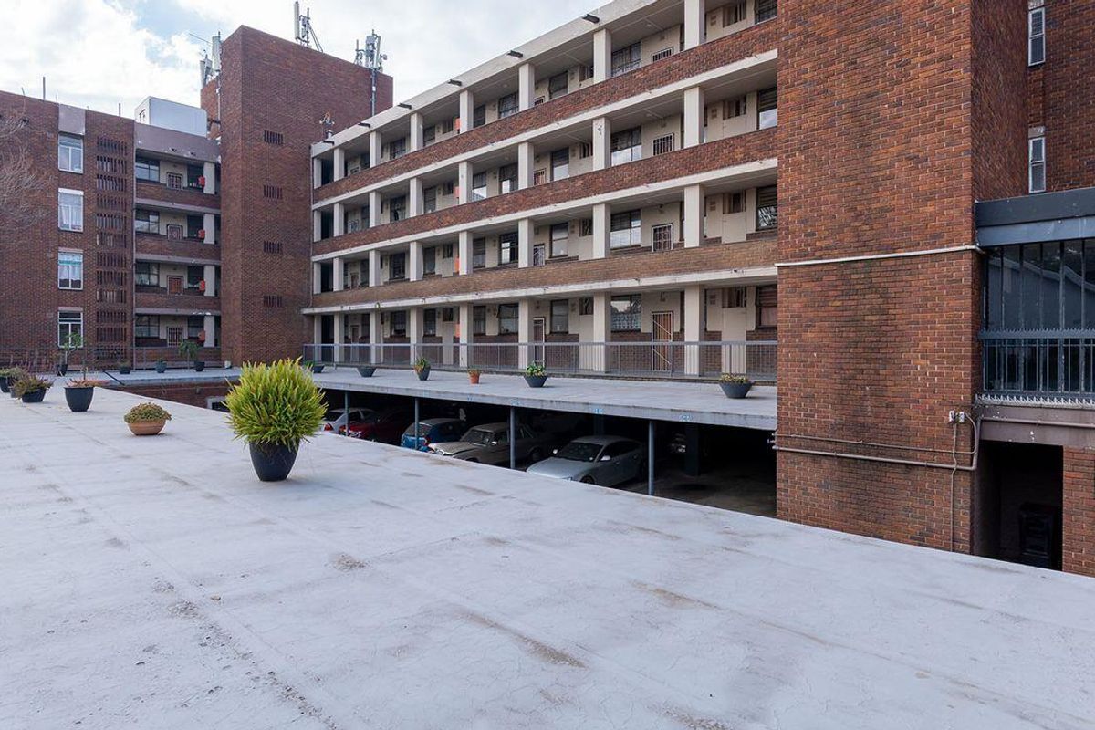 Exterior view of a multi-story brick apartment complex featuring covered parking bays and open-air walkways.