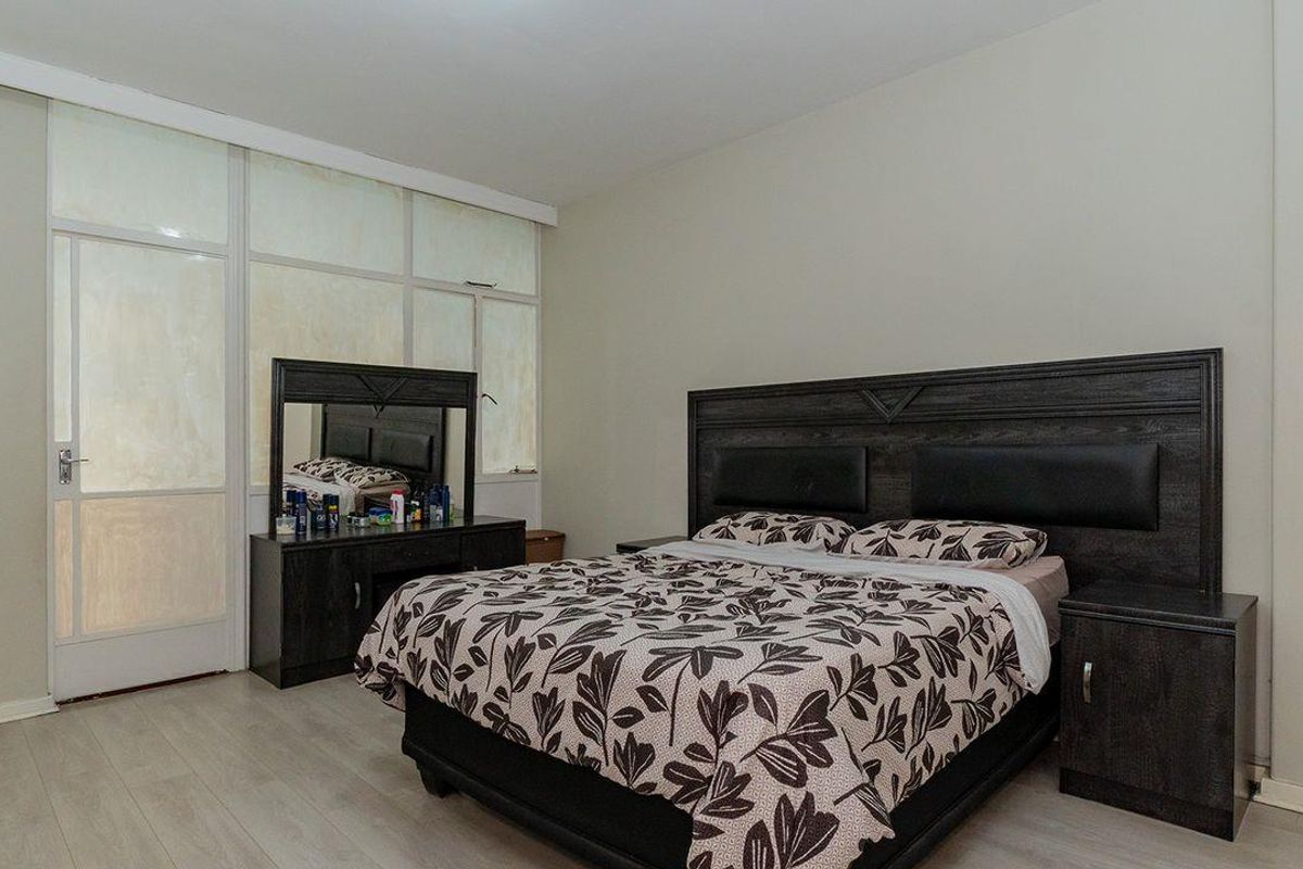 A spacious bedroom featuring light-toned laminate flooring and a large glass-paneled door providing natural light.