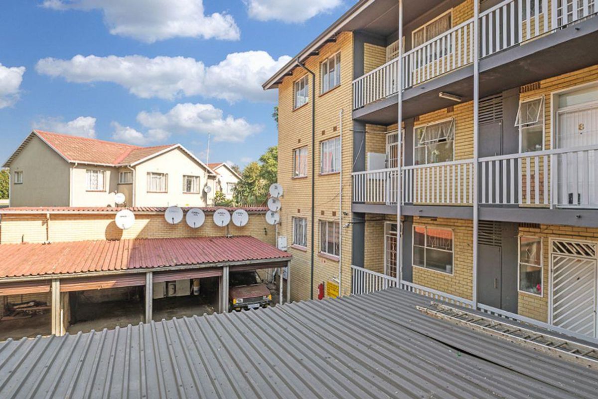Exterior view of an apartment building featuring brick facade, multiple balconies, and a covered carport area.