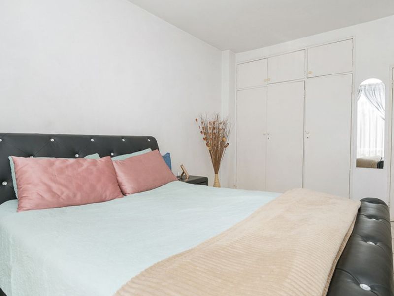 A bedroom featuring built-in cupboards, tiled flooring, and a ventilation grille, offering a functional space with potential for cosmetic updates.