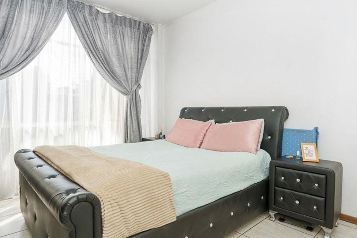 A bright bedroom featuring tiled flooring and large windows with installed curtain tracks, offering a clean and functional living space.