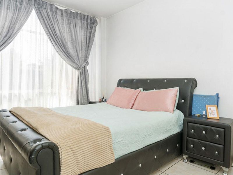 A bright bedroom featuring tiled flooring and large windows with installed curtain tracks, offering a clean and functional living space.