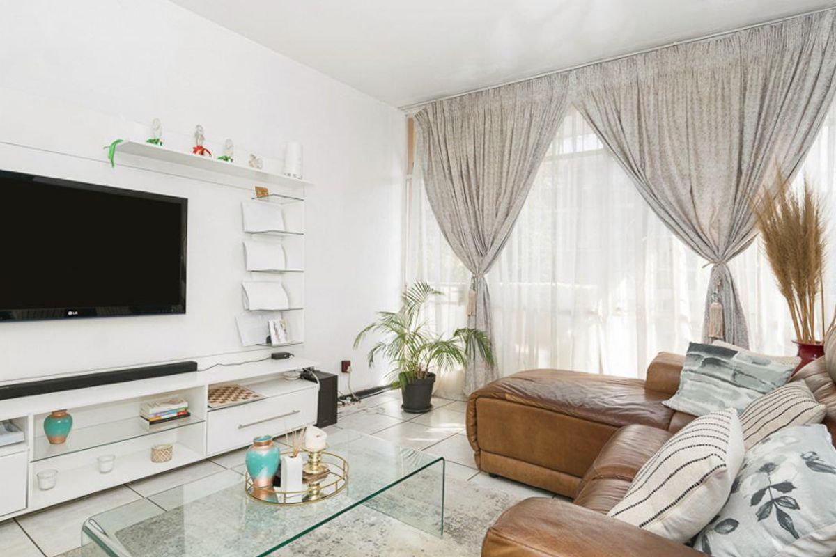 A bright living room featuring tiled flooring, a built-in media console, and large windows allowing for ample natural light.