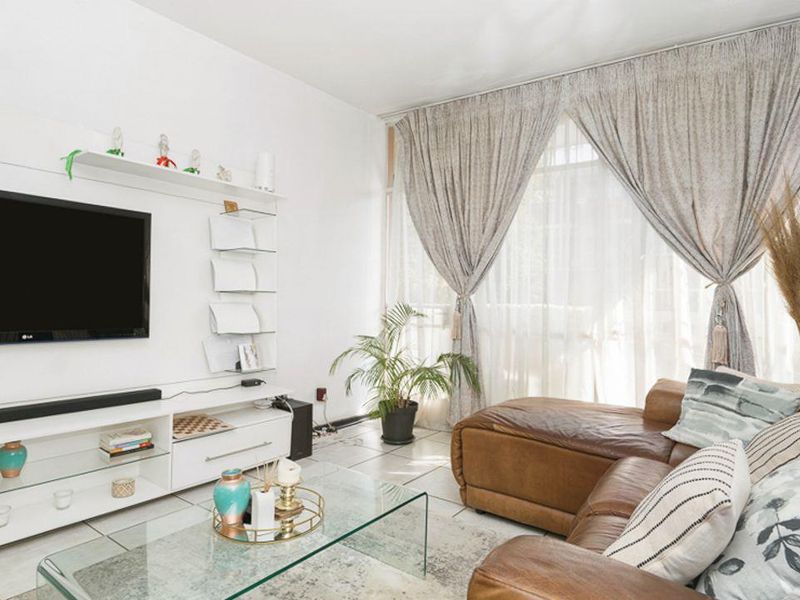 A bright living room featuring tiled flooring, a built-in media console, and large windows allowing for ample natural light.