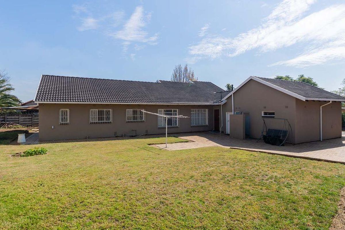 Rear view of the house featuring a paved patio area, tiled roof, and a spacious backyard with established lawn.