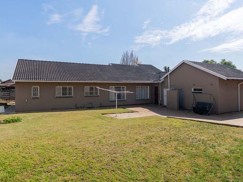 Rear view of the house featuring a paved patio area, tiled roof, and a spacious backyard with established lawn.
