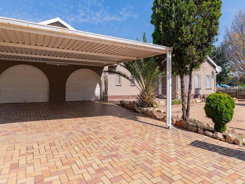 Front exterior view featuring a paved driveway, a covered carport, and double roller garage doors with security features.