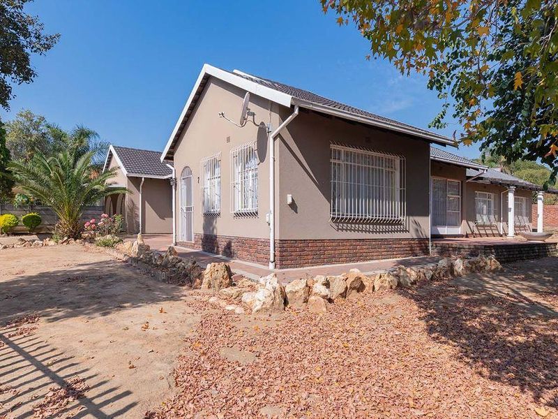 A well-maintained single-story house featuring a tiled roof, brick base detailing, and security bars on windows, set within a spacious garden area.