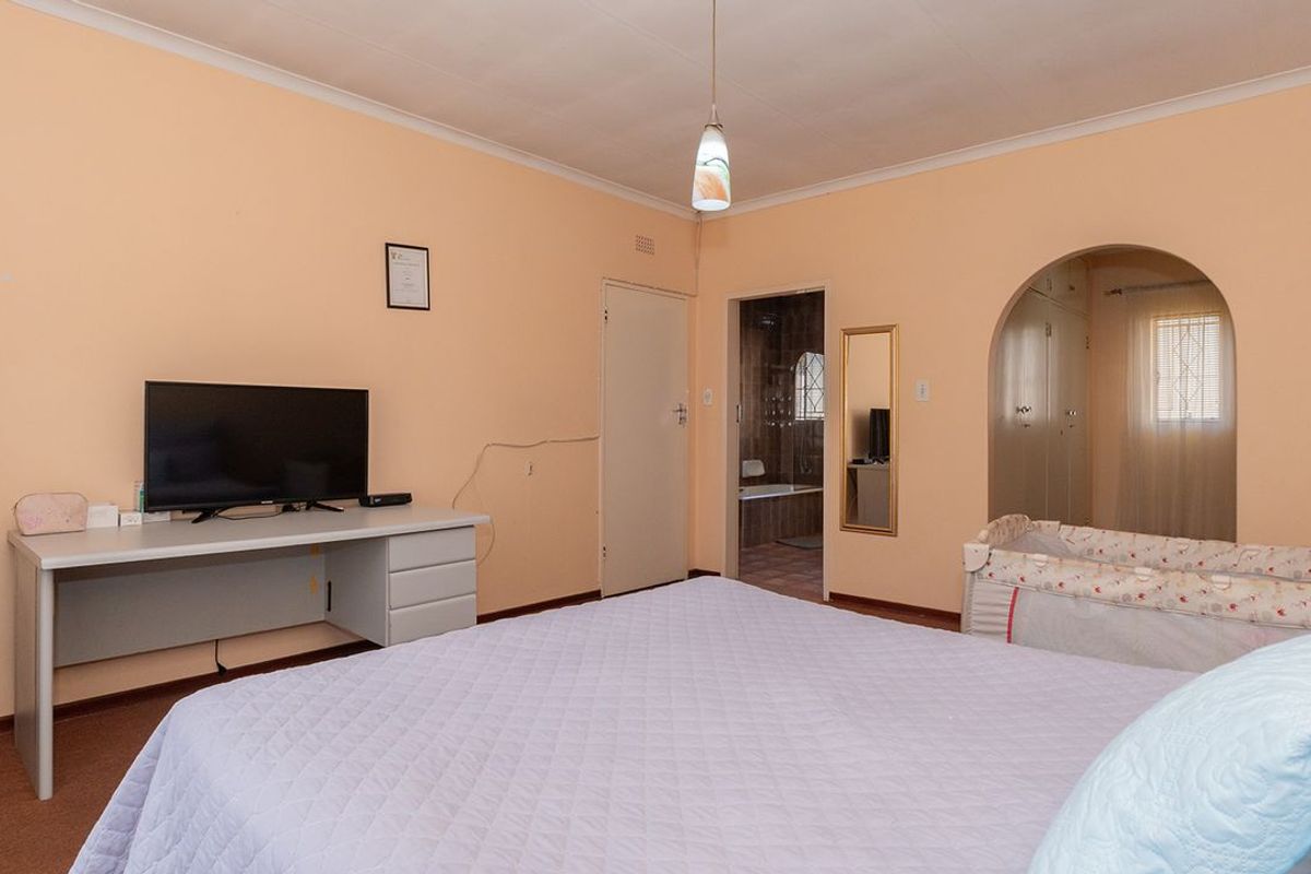 A spacious bedroom featuring built-in cupboards, an arched entryway to the en-suite bathroom, and neutral wall finishes.