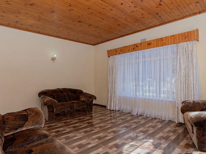 A living room featuring a timber tongue and groove ceiling, tiled flooring, and a large window with a timber pelmet.