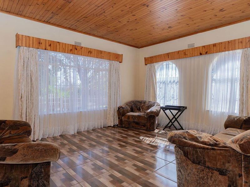A living room featuring a timber-clad ceiling, tiled flooring, and large windows with security bars and timber pelmets.