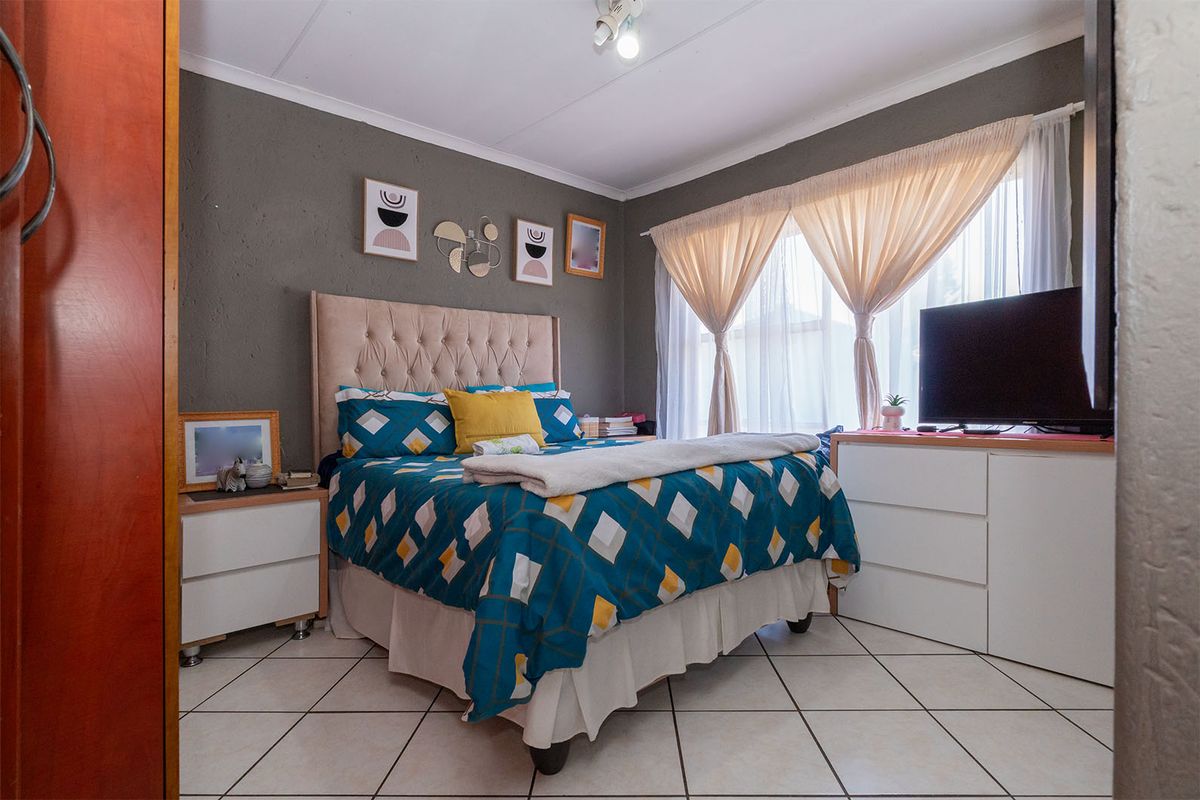 A well-lit bedroom featuring tiled flooring, a textured accent wall, and large windows with curtains, providing a comfortable living space.