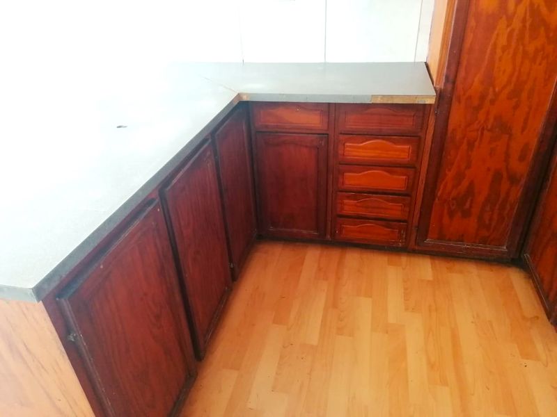 A dated kitchen area featuring traditional wood-finish cabinetry, laminate countertops, and wood-look laminate flooring, presenting an opportunity for modern renovation.