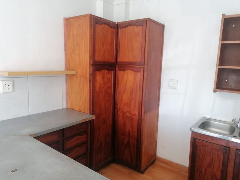 A dated kitchen area featuring built-in wooden cabinetry, laminate countertops, and a stainless steel sink, offering potential for modernization.