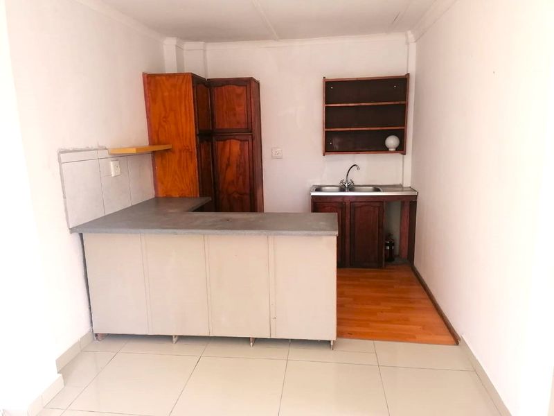 A compact kitchen area featuring built-in cabinetry, a stainless steel sink, and a mix of tiled and laminate flooring, ready for modernization.