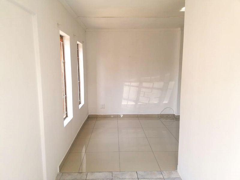 A bright, empty living area featuring neutral tiled flooring and natural light from side windows, offering a blank canvas for interior design.