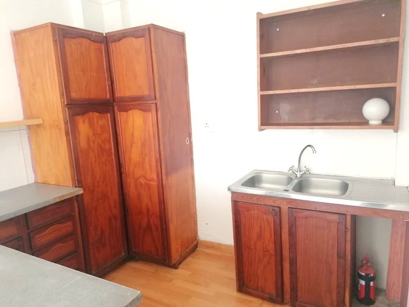A dated kitchen area featuring wooden cabinetry, open shelving, and a double bowl stainless steel sink with laminate flooring.