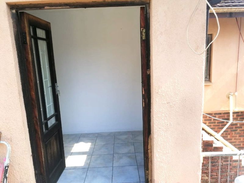 An exterior view of an entrance doorway featuring tiled flooring and a timber door frame, showing signs of wear and maintenance requirements.