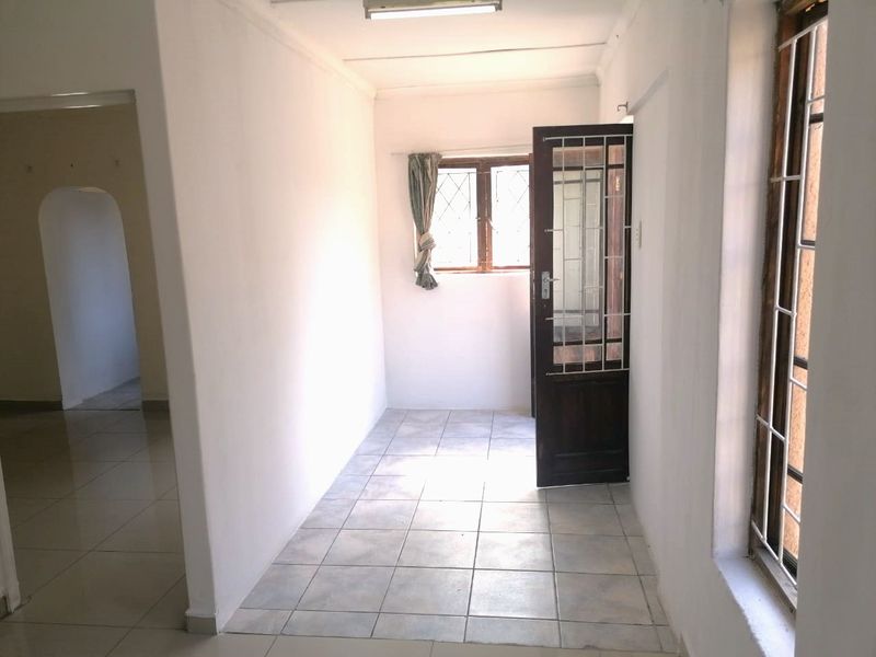 A bright, empty hallway featuring tiled flooring, security gates, and an arched entryway leading to adjacent living spaces.
