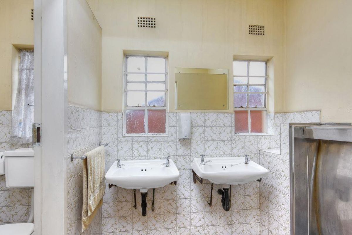 A functional bathroom featuring dual wall-mounted ceramic basins, a stainless steel urinal, and tiled wall finishes with integrated ventilation grilles.