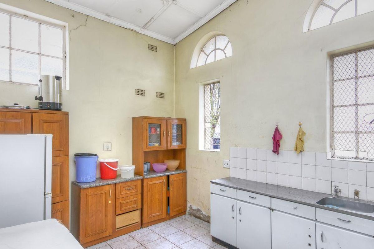 A dated kitchen featuring wooden and white cabinetry, tiled flooring, and multiple windows, requiring significant renovation and repair to the walls and finishes.