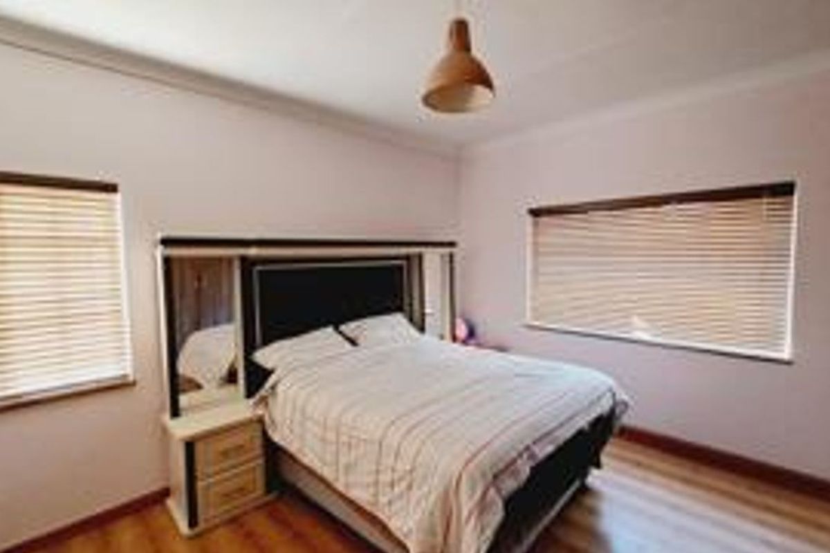 A bedroom featuring laminate flooring, coving, and dual windows fitted with venetian blinds.